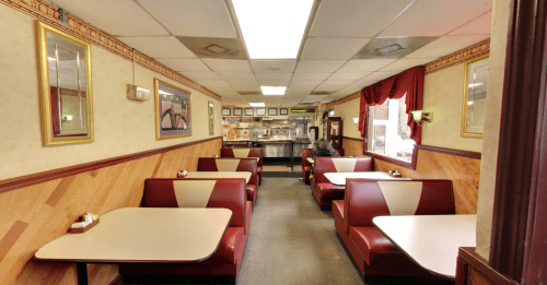 Interior of a diner featuring red and white booths, tables, and framed pictures on the walls. A counter is visible in the back.