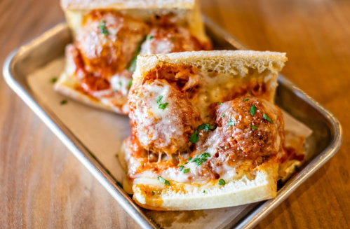 A close-up of a meatball sub sandwich with melted cheese and marinara sauce, served on a metal tray.