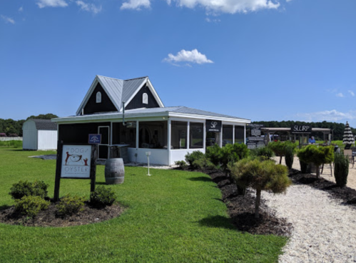 A charming restaurant with a black and white exterior, surrounded by green grass and a clear blue sky.