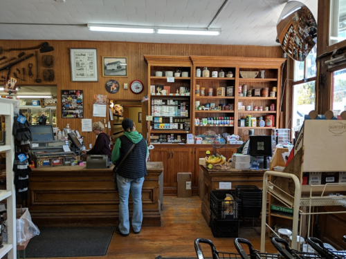 A cozy store interior with wooden shelves, a checkout counter, and a customer interacting with the cashier.