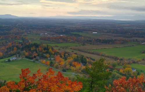 A scenic view of rolling hills and fields with vibrant autumn foliage under a cloudy sky.