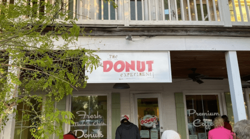 A storefront with a sign reading "The DONUT Experiment!" and people waiting outside.