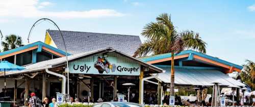 Exterior of the Ugly Grouper restaurant with colorful buildings and palm trees, bustling with outdoor diners.