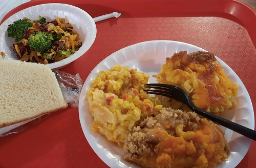 A red tray holds two plates of food: macaroni and cheese, baked dish, and a side of broccoli with a bread slice.