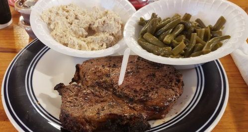 A plate with a grilled steak, a side of green beans, and a bowl of mashed potatoes.