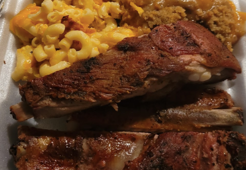 A plate of barbecue ribs with macaroni and cheese, cornbread, and a side of baked beans.