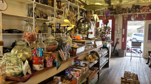 A cozy shop interior filled with jars of candy, snacks, and various vintage items on wooden shelves.