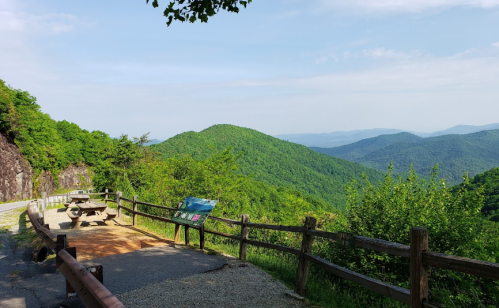 Scenic view of green mountains and a picnic area with a wooden fence under a clear blue sky.