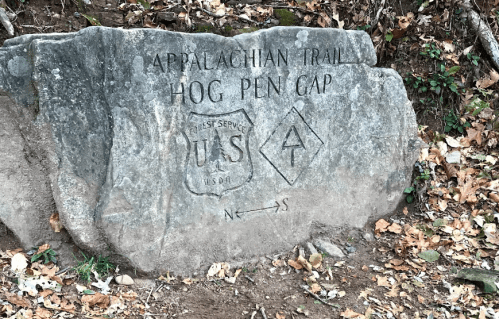 A large rock with engraved text marking the Appalachian Trail and Hog Pen Gap, surrounded by fallen leaves.