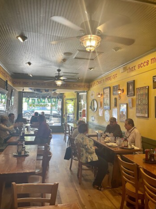 Cozy restaurant interior with wooden tables, ceiling fans, and patrons enjoying meals in a warm, inviting atmosphere.