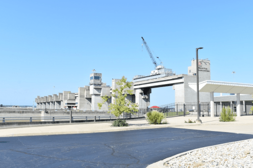 A concrete dam structure with a crane, blue sky, and a paved area in the foreground.