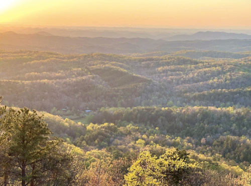 A scenic view of rolling hills and valleys at sunset, with warm golden light illuminating the landscape.