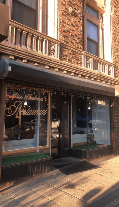 Exterior of Miss Thelma's Restaurant, featuring a brick facade and large windows with decorative signage.