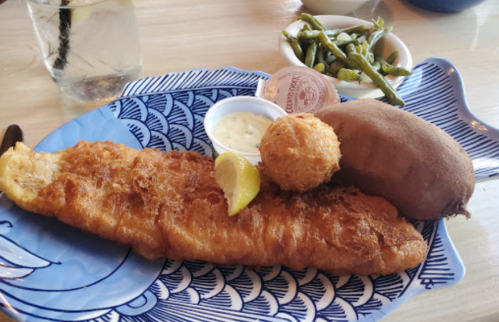 A plate featuring a large fried fish fillet, a sweet potato, a hushpuppy, and a side of green beans.