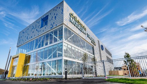 Modern building of a children's museum with large glass windows and a bright yellow entrance, set against a blue sky.