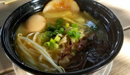 A bowl of ramen with broth, noodles, green onions, bean sprouts, a soft-boiled egg, and slices of meat.