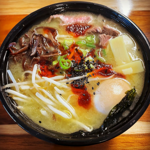 A bowl of ramen with broth, noodles, sliced beef, vegetables, a soft-boiled egg, and chili paste on top.