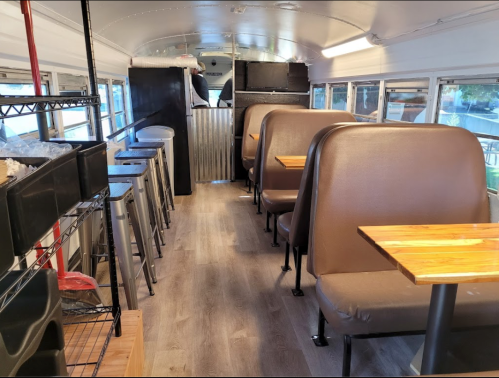 Interior of a converted bus with wooden tables, seating booths, and a clean, modern design.