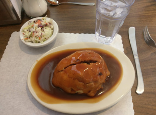 A plate with a large, saucy meat dish, served with a side of coleslaw and a glass of water.