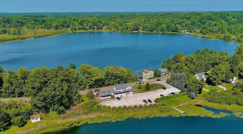 Aerial view of a serene lake surrounded by greenery, with a small building and parking area along the shore.