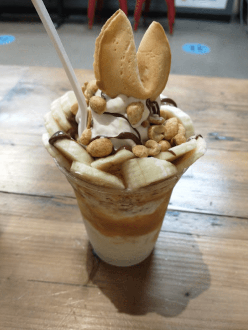 A delicious dessert with layers of ice cream, banana slices, chocolate drizzle, and topped with a cookie and peanuts.
