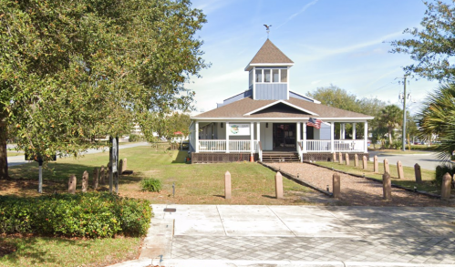 A charming building with a peaked roof, surrounded by greenery and a pathway, featuring an American flag.