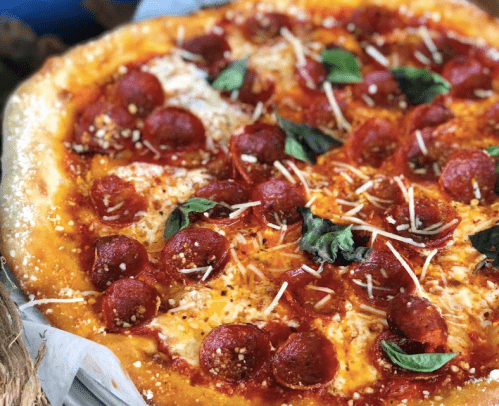 A close-up of a pepperoni pizza topped with cheese and fresh basil leaves.