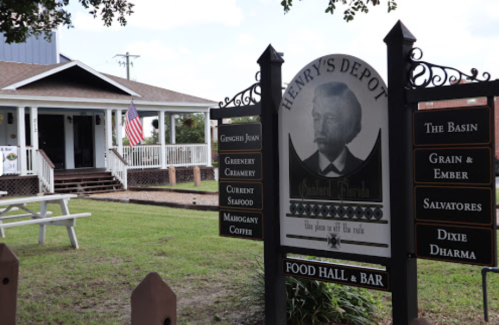 Sign for Henry's Depot, featuring dining options and a historic building with an American flag in the background.