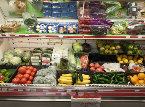 A colorful display of fresh fruits and vegetables in a grocery store, including tomatoes, lettuce, apples, and cucumbers.