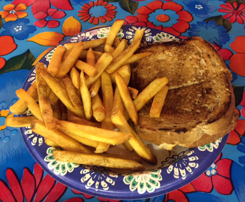 A plate of golden French fries next to a toasted sandwich on a colorful floral tablecloth.