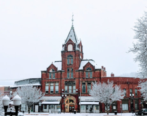 Historic brick building with a tower, surrounded by snow-covered trees, in a winter landscape.