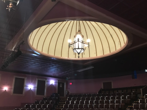 Interior of a theater featuring a circular ceiling with a chandelier and rows of empty seats below.