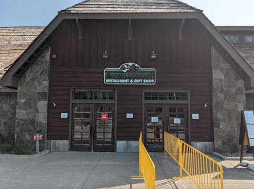 Exterior of Annie Creek Restaurant & Gift Shop, featuring a wooden facade and double glass doors with a yellow barrier.