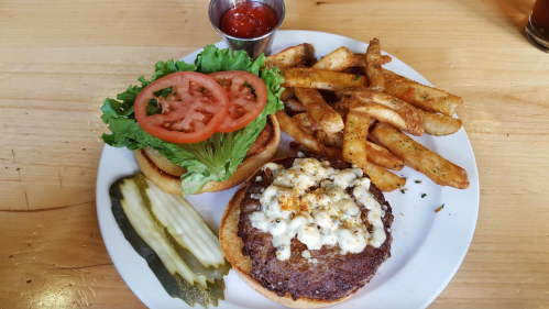 A plate with a burger topped with cheese, lettuce, and tomato, served with fries and pickles on the side.