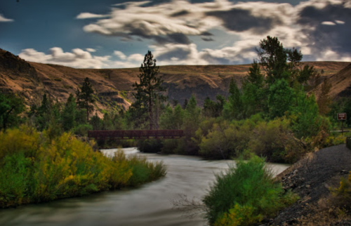 A serene river flows through a lush landscape, framed by hills and trees under a cloudy sky.