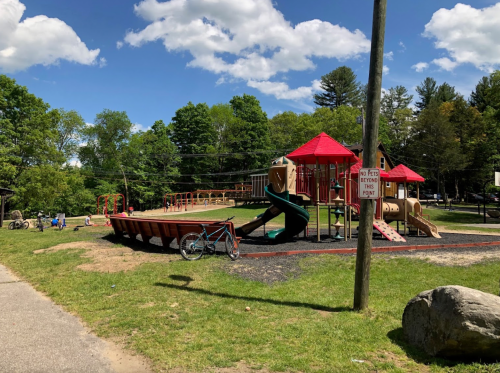 A playground with slides and climbing structures, surrounded by trees and a grassy area, with a bike nearby.