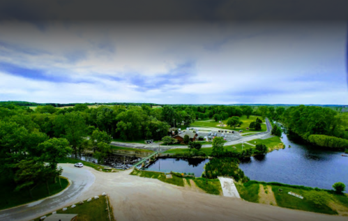 A scenic view of a river surrounded by lush greenery and a parking area, under a cloudy sky.