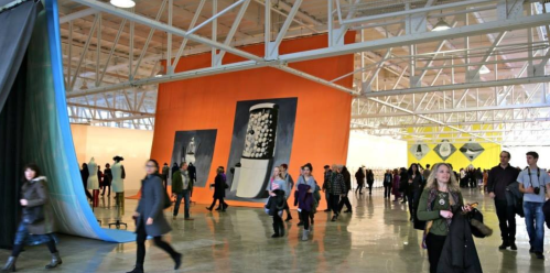 A spacious art gallery with colorful walls and visitors walking through, admiring the exhibits.