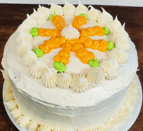 A round cake with white frosting, decorated with orange and green icing in a floral pattern on top.