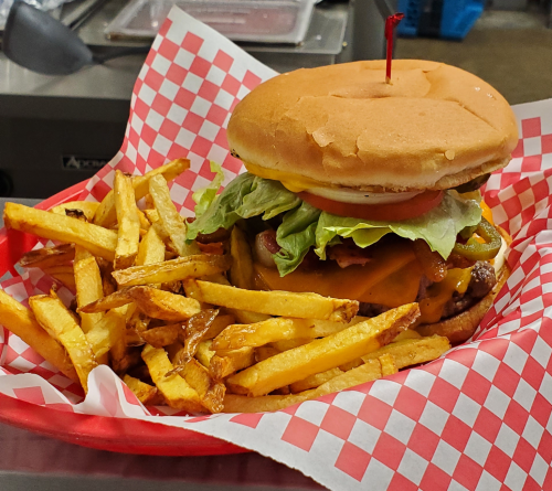 A juicy burger with lettuce, tomato, and cheese, served with a side of golden fries in a red-checkered basket.