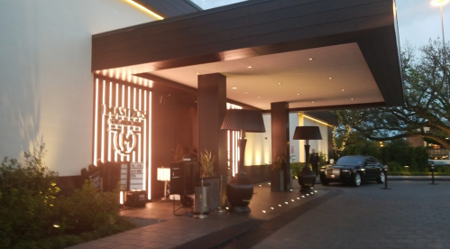 Exterior view of a modern building entrance with stylish lighting and landscaping, featuring a parked car.