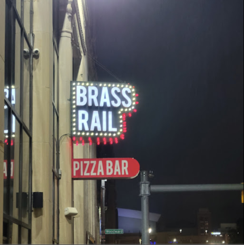 Neon sign for "Brass Rail Pizza Bar" illuminated at night, hanging from a building.