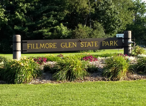 Sign for Fillmore Glen State Park surrounded by greenery and colorful flowers.