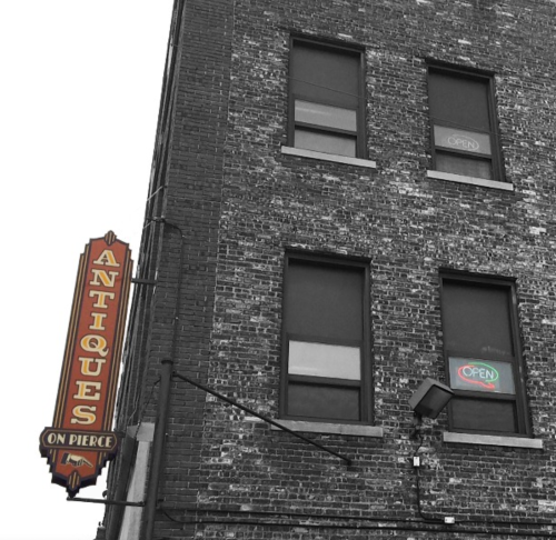 A brick building with a vintage "Antiques on Pierce" sign and an "Open" neon sign in the window.