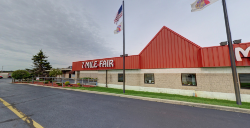 Exterior view of the 7 Mile Fair building with flags flying and a cloudy sky in the background.
