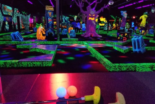 A vibrant glow-in-the-dark mini-golf course with colorful decorations and two golf balls in the foreground.
