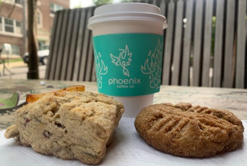 A coffee cup from Phoenix Coffee Co. next to a scone and a cookie on a napkin, set on a wooden table.