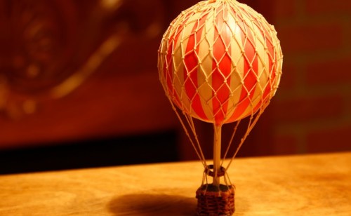 A small decorative hot air balloon model with a red and white pattern, sitting on a wooden surface.