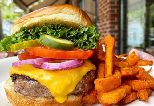 A juicy cheeseburger with lettuce, tomato, pickles, and onion, served with crispy sweet potato fries.