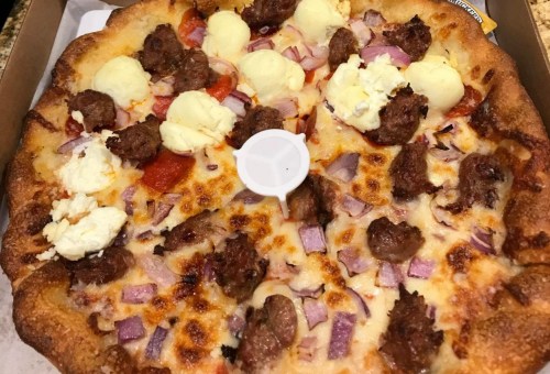 A pizza topped with sausage, pepperoni, red onions, and dollops of creamy cheese on a golden crust.